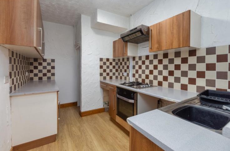Original tired kitchen with brown units and checkered tile splashback